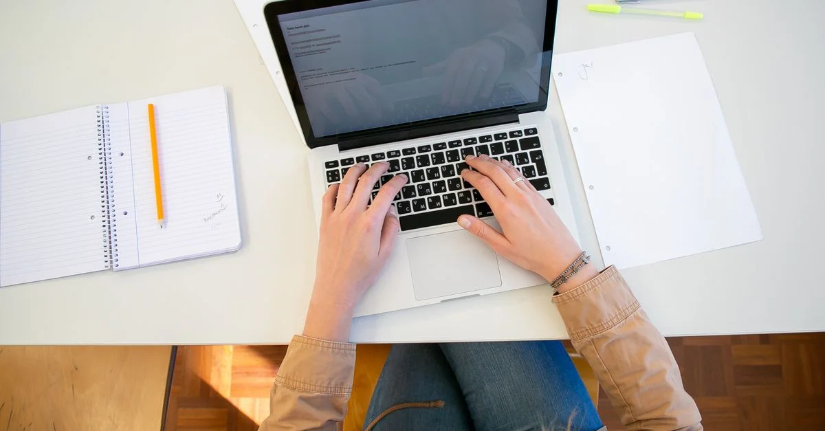Vue en plongée d'une étudiante tapant sur un ordinateur portable entourée de notes.