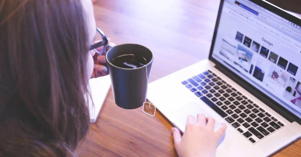 Une femme savoure un café tout en naviguant sur le web sur un ordinateur portable à un bureau à domicile.