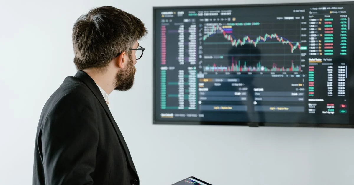 Homme observant les données du marché boursier sur un écran et tenant une tablette, représentant l'analyse financière et le trading.
