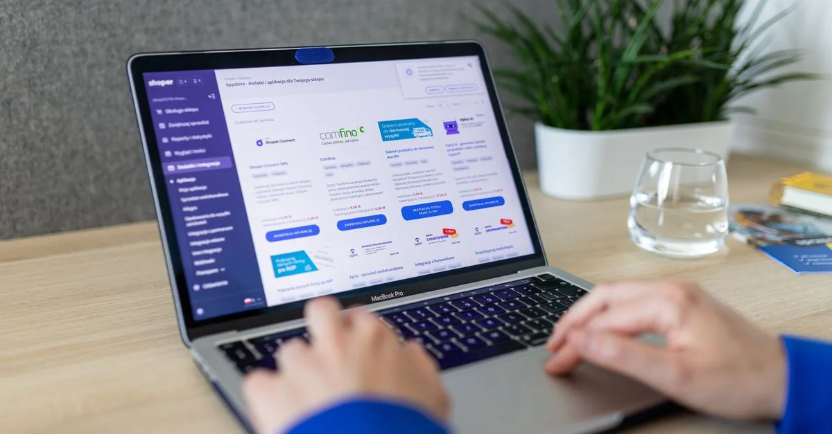 Gros plan sur des mains sur un ordinateur portable naviguant sur un site e-commerce dans un bureau moderne.
