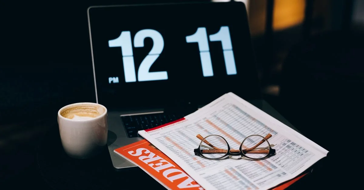 Un espace de travail avec un ordinateur portable, une tasse de café, des papiers et des lunettes dans un environnement professionnel.