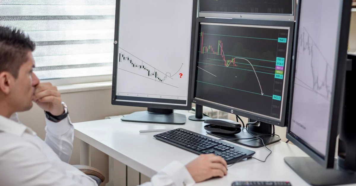 Professionnel des affaires analysant des données financières sur plusieurs moniteurs à son espace de travail.